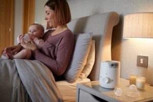 Image of mum feeding baby in bed with Tommee Tippee Bottle Warmer at the bedside